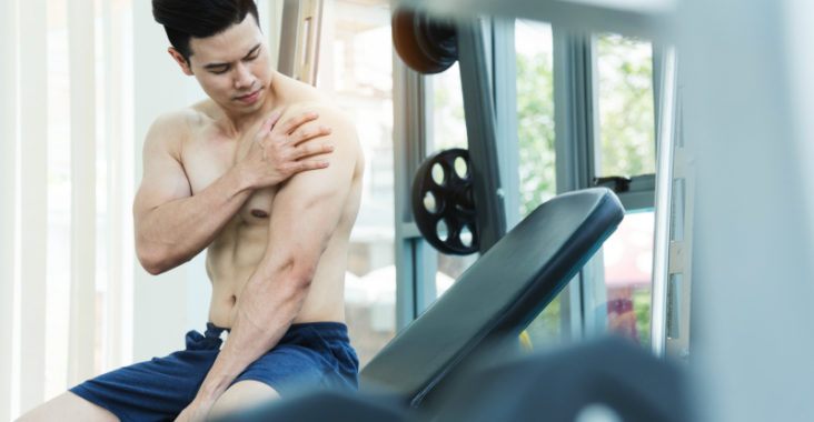 Bodybuilder sitzt auf Schrägbank und great auf seine schmerzende Schulter.