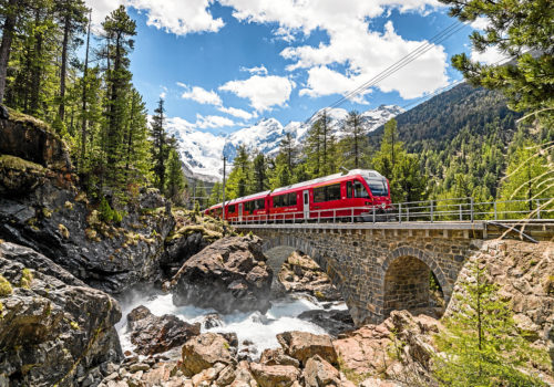 Via Albula/Bernina in Graubünden: Die Rhätische Bahn überquert ein Viadukt inmitten einer frühlingshaften Naturlandschaft. © Rhätische Bahn